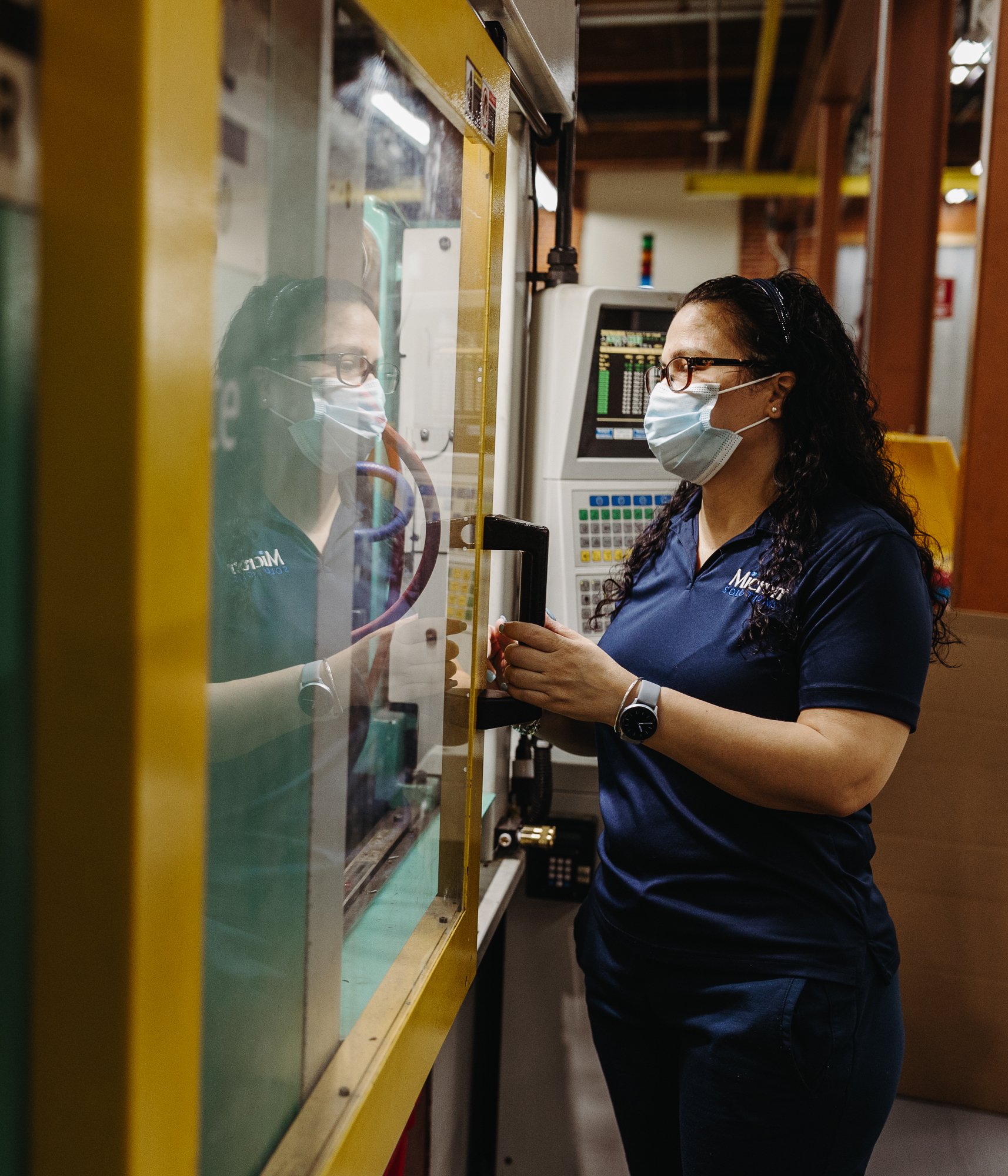 An employee in a blue Micron polo shirt opens the door to an injection molding machine.