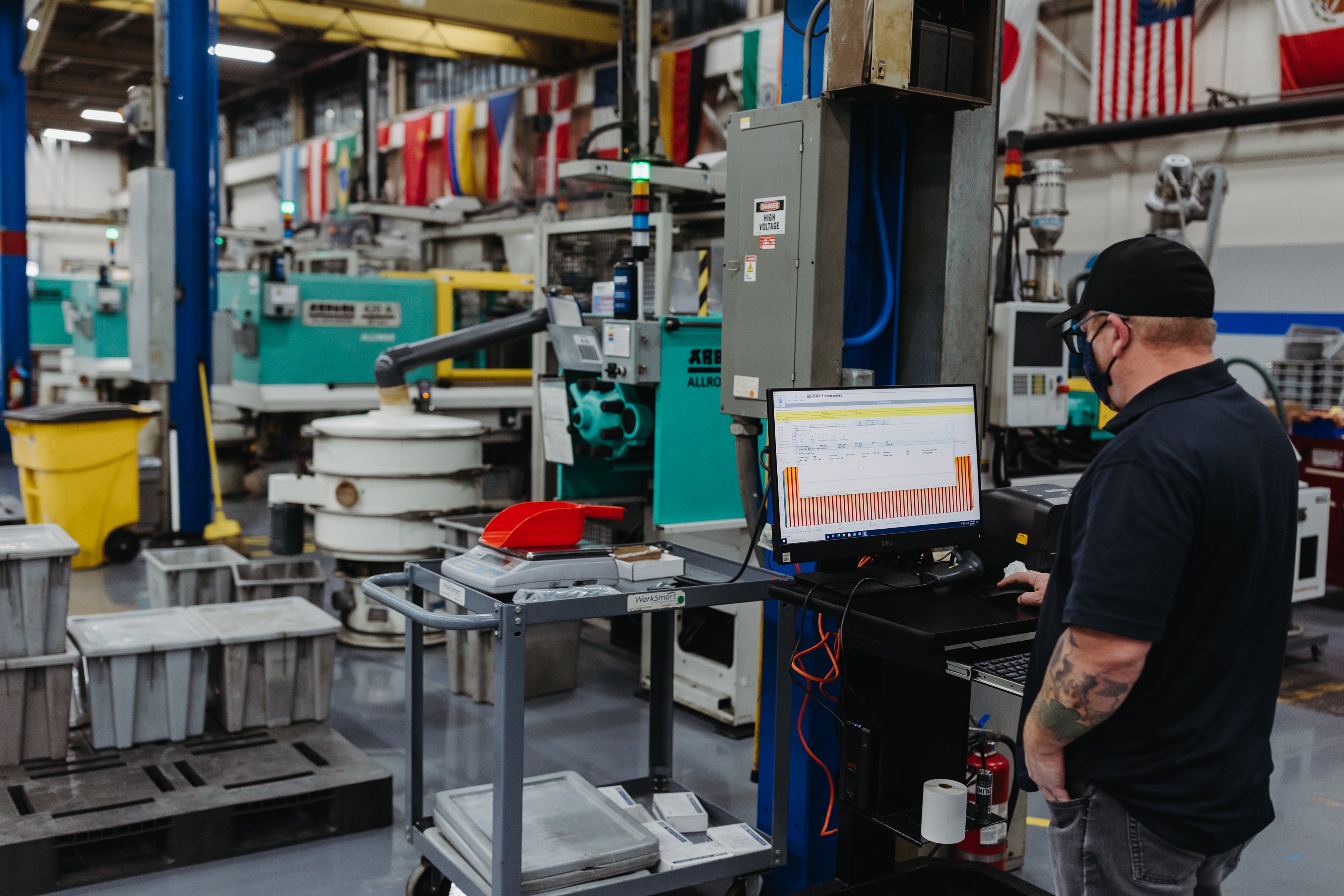 A man (facing away from the camera) looks at a computer screen which shows the status of the injection molding machines