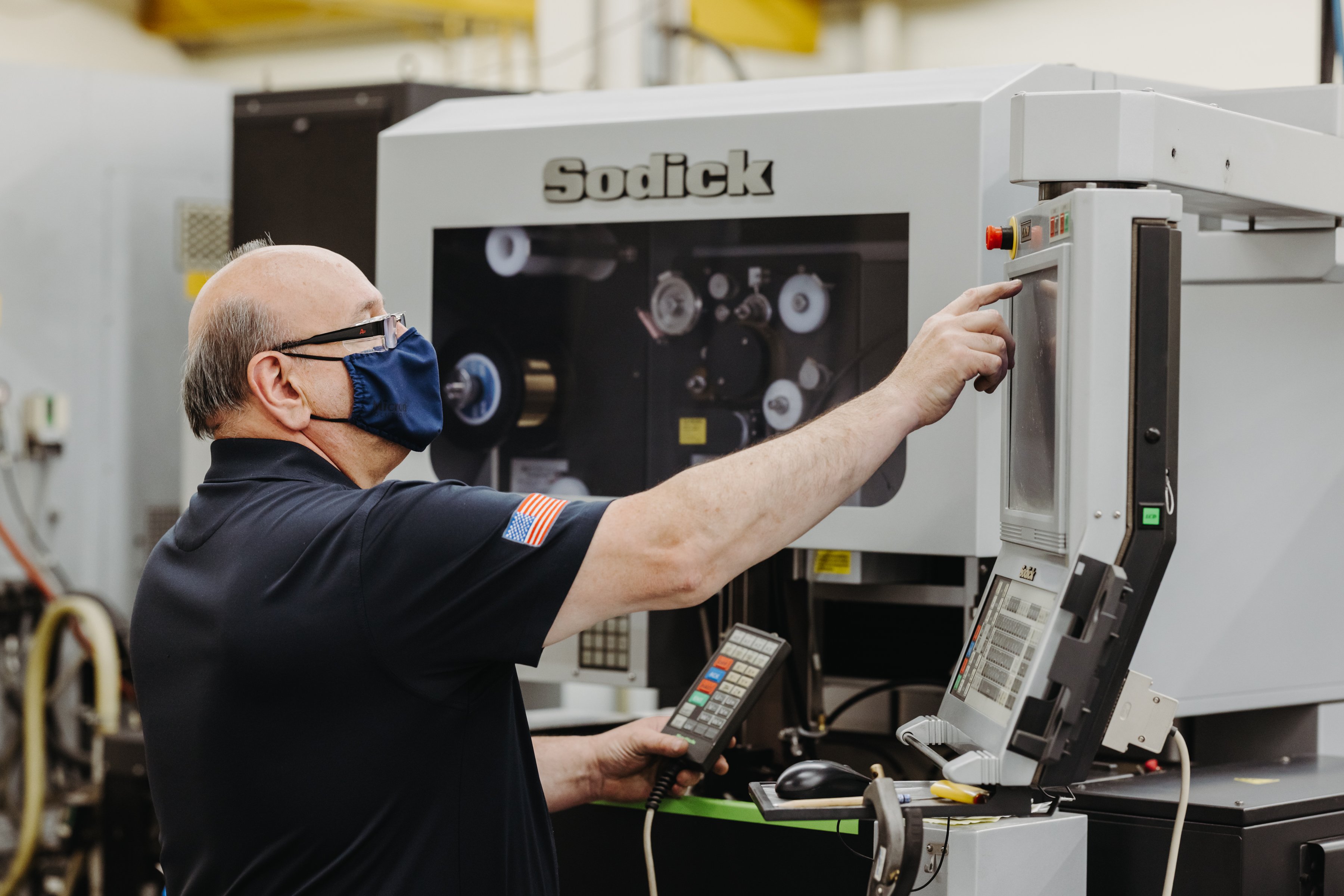 A man wearing a blue mask points to the screen on a Sodick CNC machine