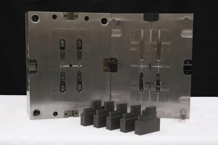 A metal mold standing behind 5 black injection-molded components made at Micron.