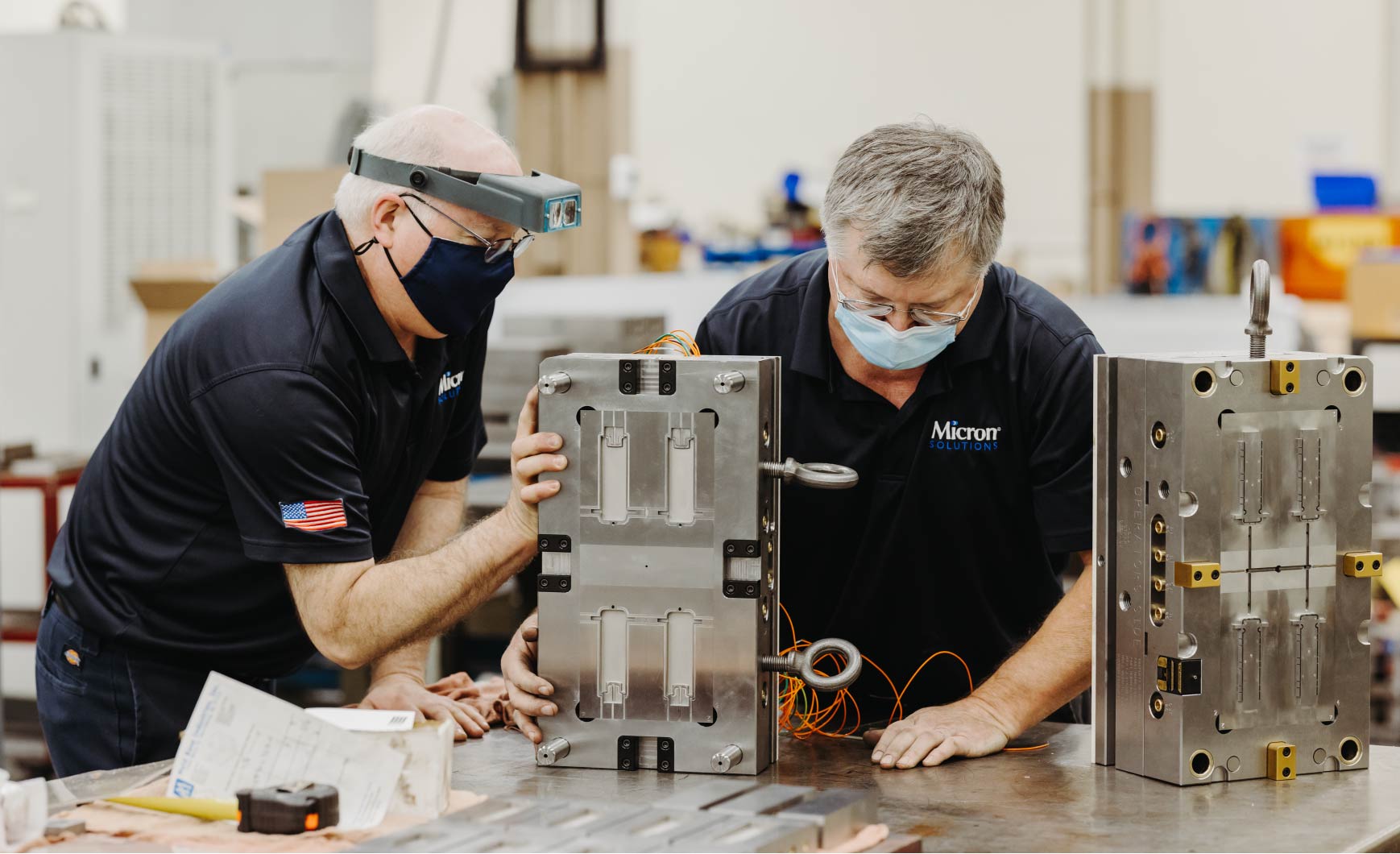 Two men wearing masks work on a mold